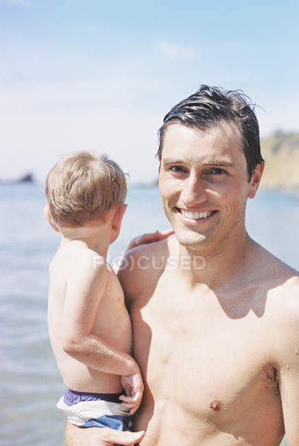 Homme portant son fils sur la plage — Photo de stock