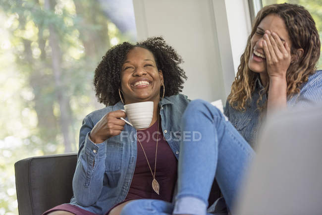 Жінки сидять на дивані, сміючись разом — стокове фото