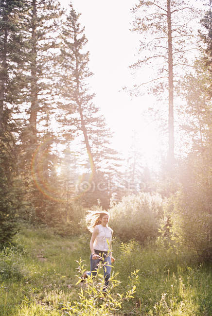 Mulher correndo através de uma floresta iluminada pelo sol . — Fotografia de Stock