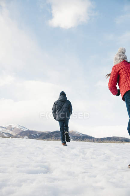 Irmão e irmã correndo através da neve . — Fotografia de Stock