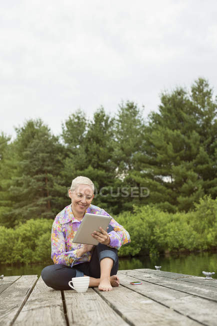 Женщина сидит на причале с помощью планшета — стоковое фото