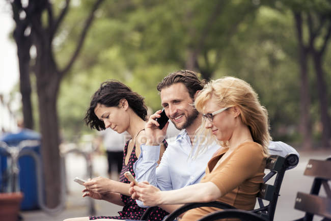Мужчина и две женщины на своих телефонах — стоковое фото