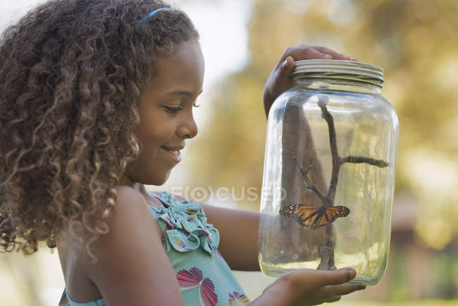 Niña sosteniendo un frasco de vidrio con una mariposa - foto de stock
