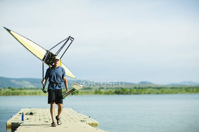 Man carrying oars and a rowing shell — Stock Photo