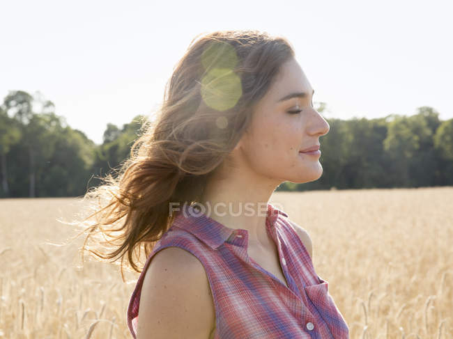 Mujer de pie en un campo de trigo maduro alto - foto de stock