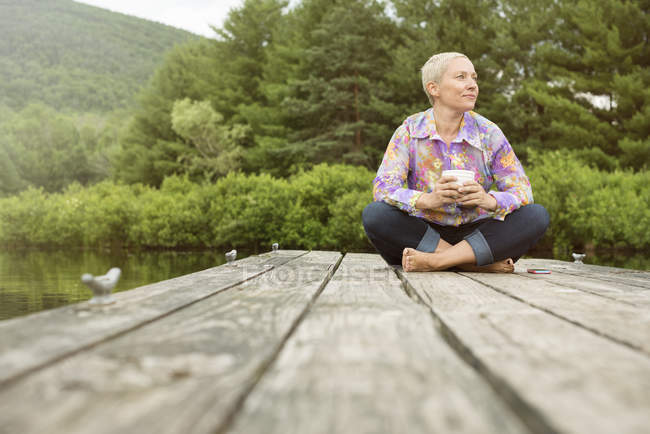 Woman sitting on a dock with cup of coffee — Stock Photo
