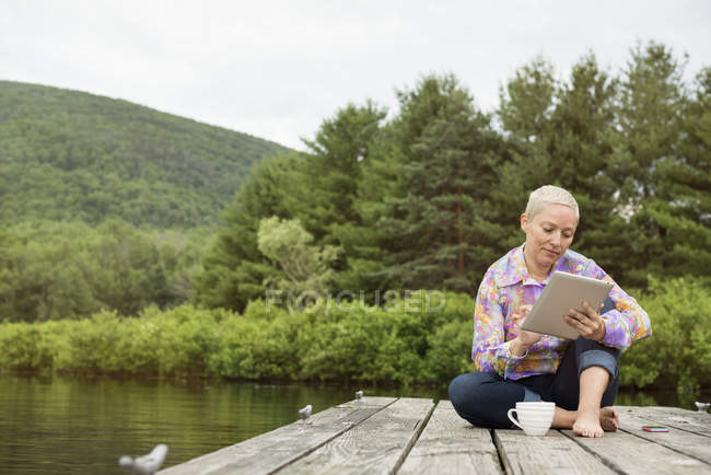 Femme assise sur la jetée en utilisant une tablette — Photo de stock