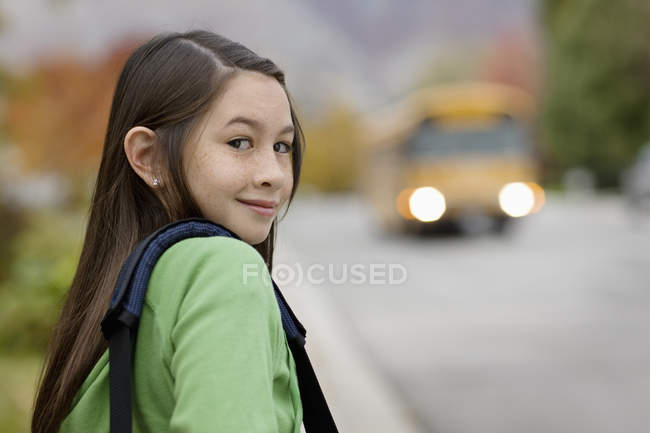 Девушка на тротуаре ждет школьный автобус — стоковое фото