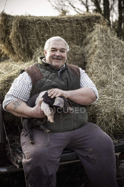 Фермер держит поросенка и улыбается — стоковое фото