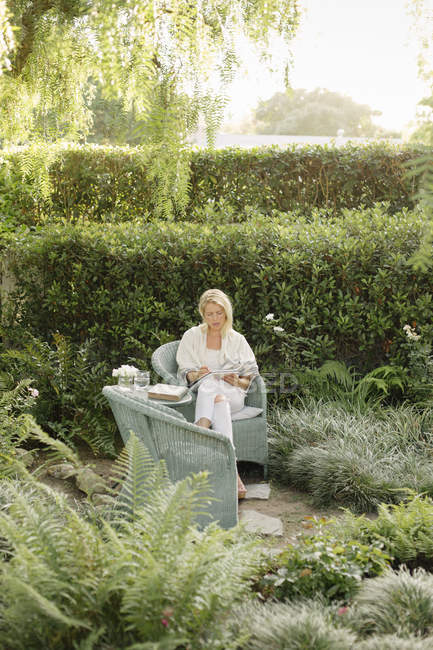 Donna seduta in un giardino, scrivendo . — Foto stock