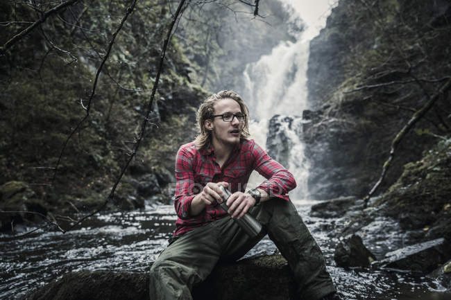 Man sitting on a rock by a waterfall — Stock Photo