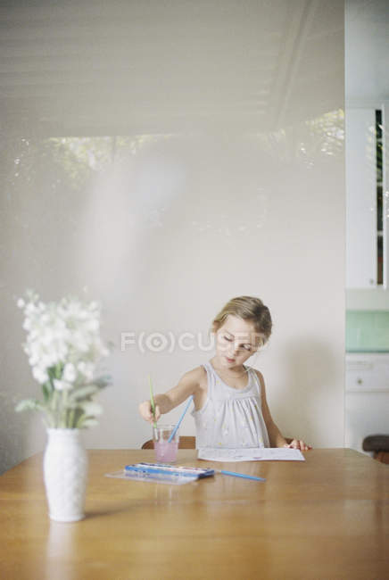 Jeune fille assise à une table, peignant — Photo de stock
