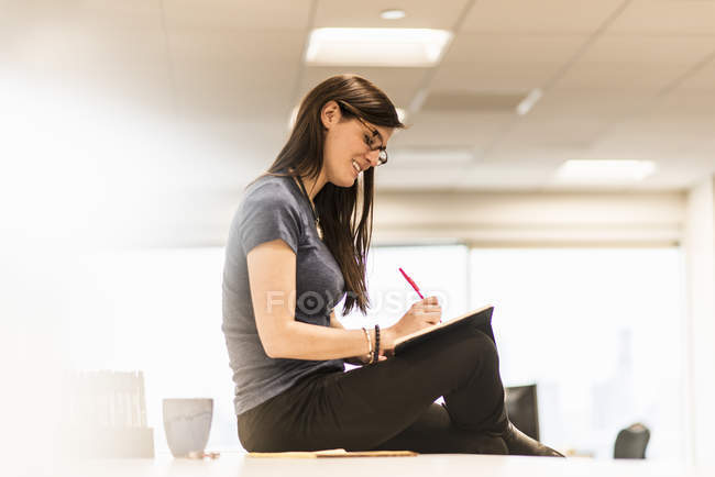 Jeune femme assise sur son bureau — Photo de stock