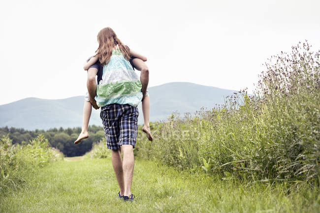 Homme donnant un enfant un piggyback dans une prairie — Photo de stock