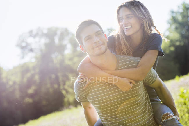 Man giving woman a piggyback on meadow — Stock Photo