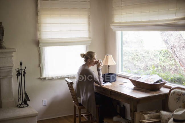 Mulher sentada em uma mesa por uma janela — Fotografia de Stock