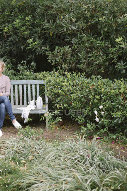 Femme assise sur un banc en bois dans un jardin — Photo de stock