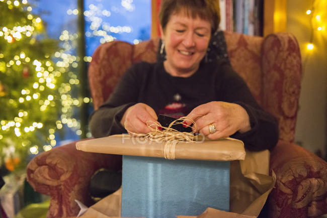 Reife Frau öffnet einen Stapel von Geschenken. — Stockfoto