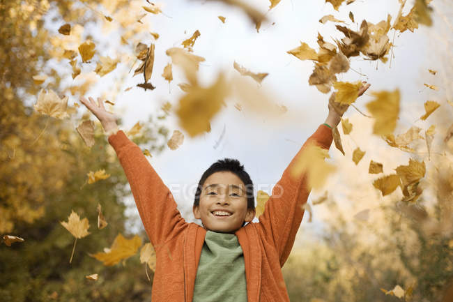 Niño lanzando hojas de otoño en el aire - foto de stock