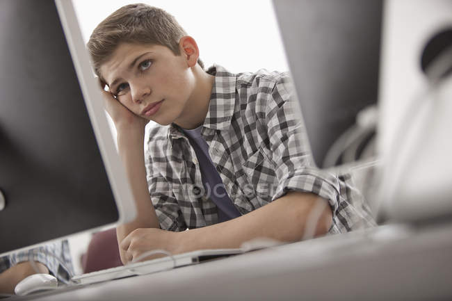 Niño sentado con la mano en la barbilla - foto de stock