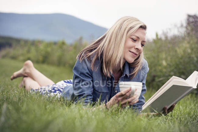 Mulher deitada na grama lendo um livro — Fotografia de Stock
