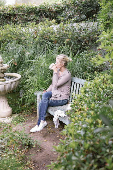 Женщина сидит на деревянной скамейке в саду — стоковое фото