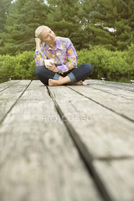 Donna seduta su un molo con una tazza di caffè — Foto stock