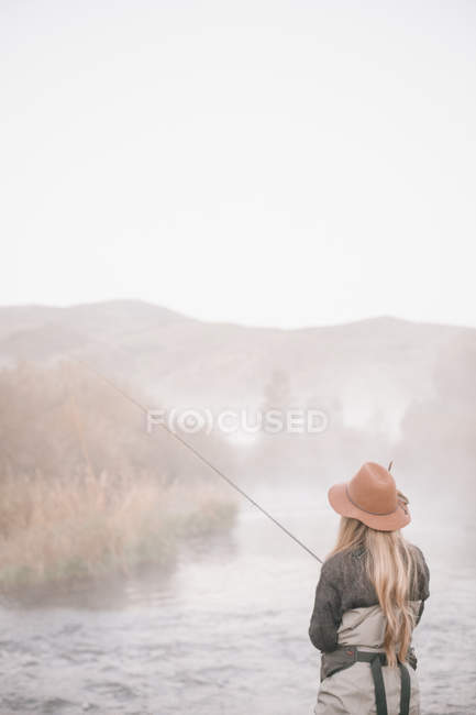 Pescadora de pie a orillas de un río - foto de stock