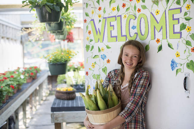 Girl with corn cobs by the Welcome sign. — Stock Photo