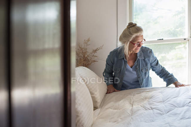 Mujer que compone la cama en el dormitorio - foto de stock
