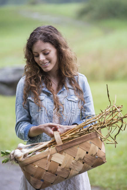 Woman carrying basket of garlic and vegetables — Stock Photo