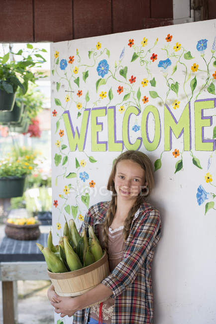 Girl with corn cobs by the Welcome sign. — Stock Photo