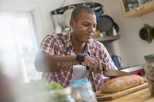 Hombre rebanando una barra de pan . - foto de stock