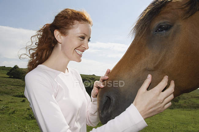 Donna accarezzare il muso di un cavallo baia . — Foto stock