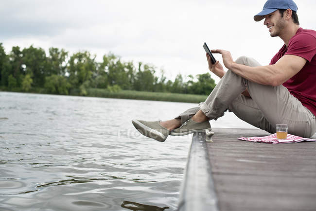 Uomo seduto su un molo vicino a un lago — Foto stock