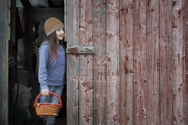 Girl in barn doorway with basket. — Stock Photo