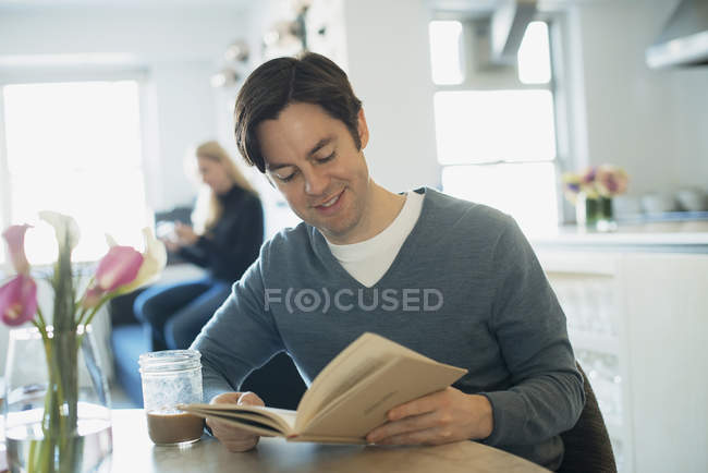 Hombre leyendo, mujer usando smartphone - foto de stock