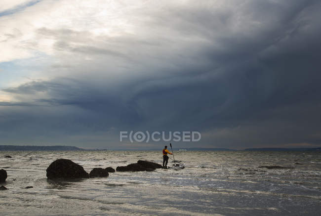 Hombre se para en una roca en kayak - foto de stock