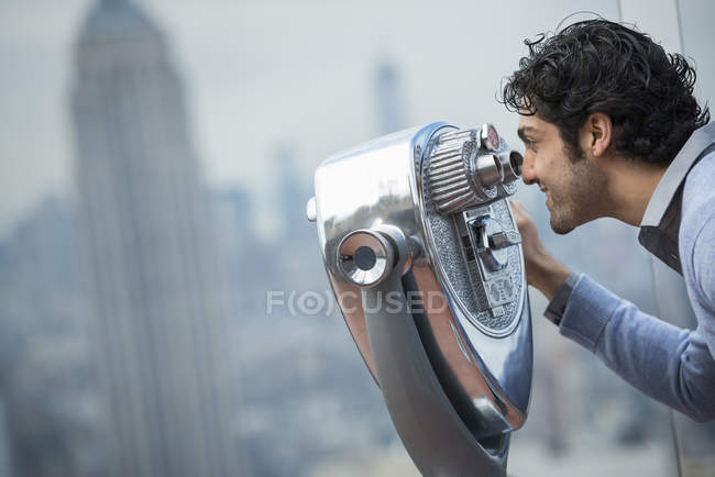 Hombre mirando a través de un telescopio sobre la ciudad
. - foto de stock