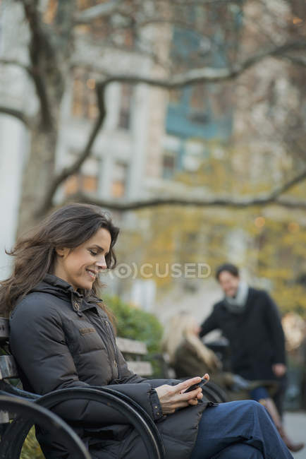 Mujer en parque urbano con smartphone - foto de stock