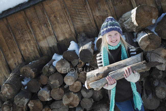 Ragazza che raccoglie legna da ardere dal mucchio di tronchi . — Foto stock