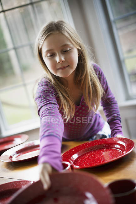 Menina que coloca a mesa com pratos — Fotografia de Stock