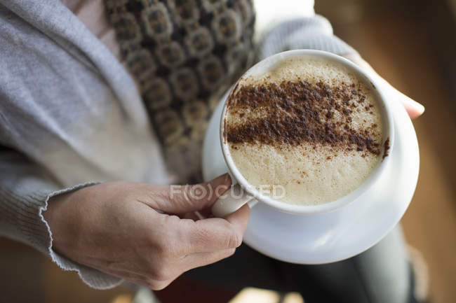 Mulher segurando uma xícara cheia de cappuccino — Fotografia de Stock