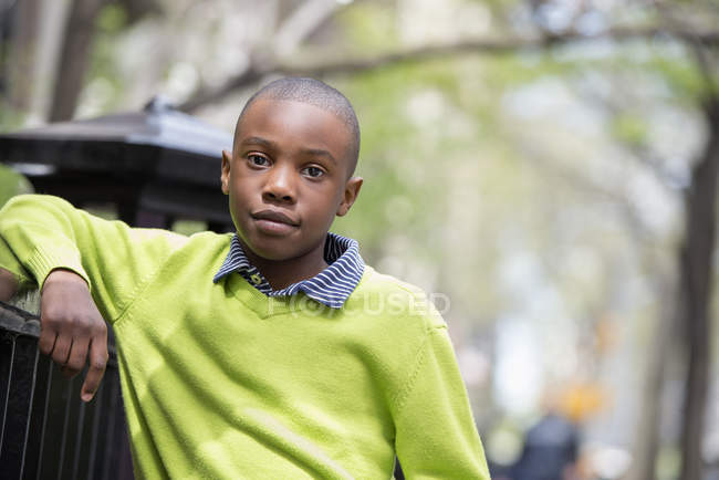 Menino de camisola verde encostado na cerca — Fotografia de Stock