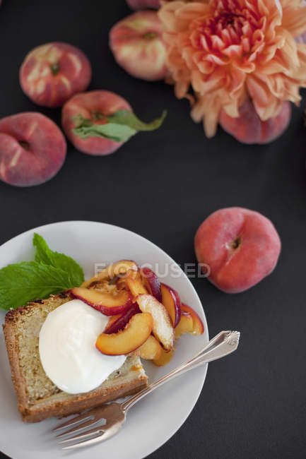Тарелка со сливочным тортом и персиками — стоковое фото