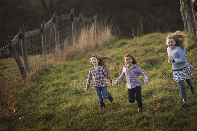 Tres niños corriendo por una colina - foto de stock