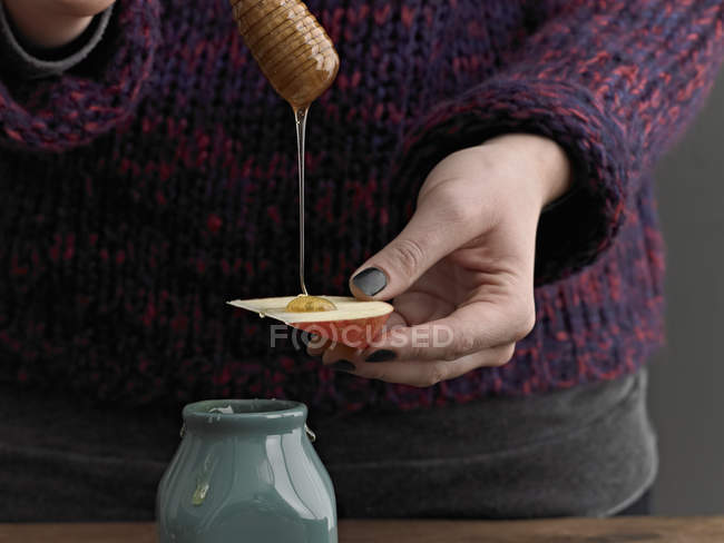 Mujer llovizna miel en rodaja de manzana - foto de stock