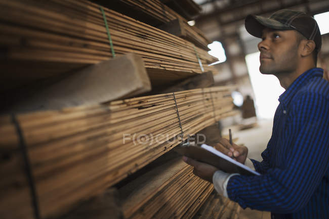 Man with a clipboard by a rack of planks. — Stock Photo