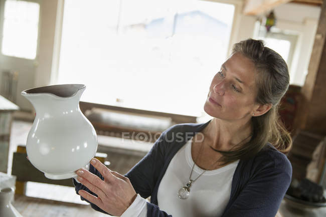 Mujer sosteniendo una jarra de cerámica blanca - foto de stock
