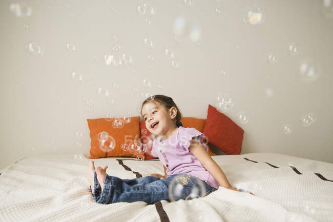 Дівчина на ліжку сміється з мильних бульбашок — стокове фото